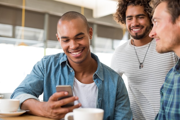 Cheerful man using smartphone at coffee shop with his friends