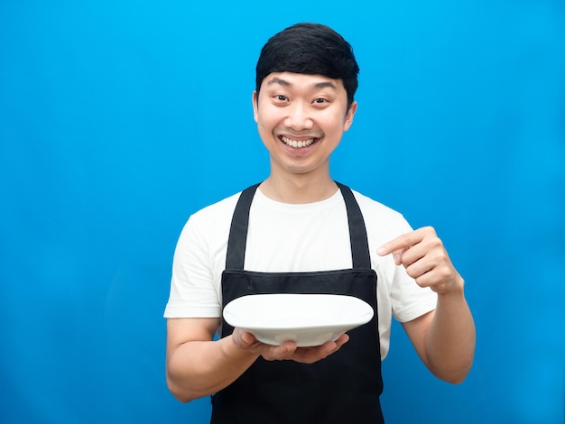 Cheerful man wearing apron point finger at dish in happiness smile blue background