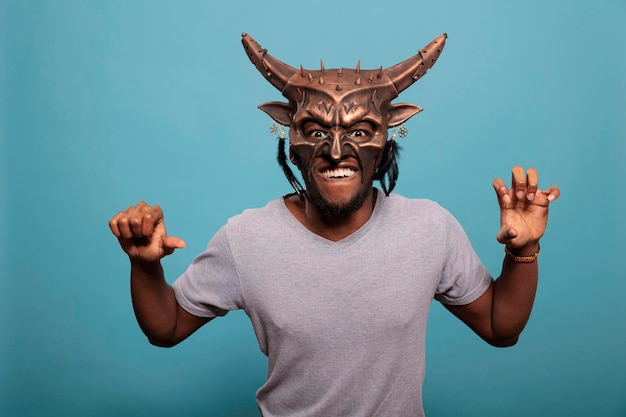 Cheerful man wearing tribal native ceremonial face mask used in indigenous culture and history to create ancient ritual. African american guy with traditional and cultural shaman object.