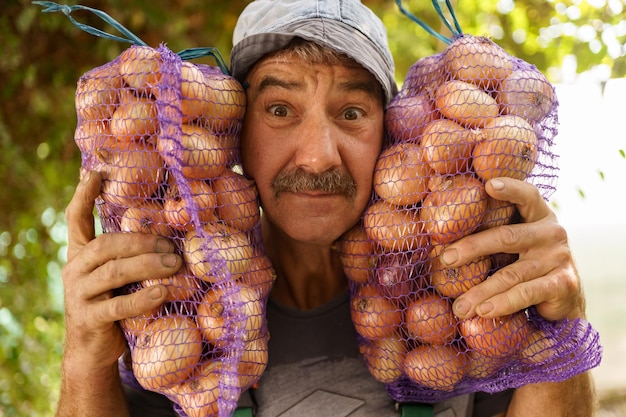 A cheerful man with two bags of onions Charismatic senior farmer holding sacks with onions