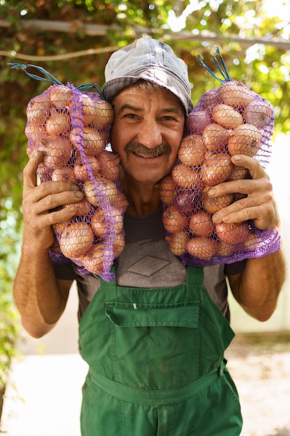 A cheerful man with two bags of onions Charismatic senior farmer holding sacks with onions