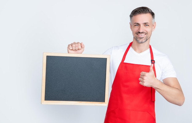 Cheerful mature man in apron hold blackboard with copy space thumb up