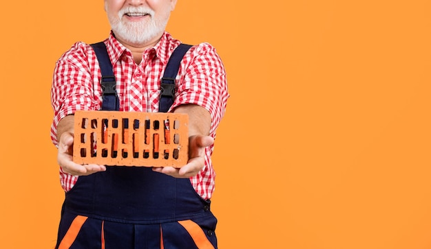 Cheerful mature man bricklayer in helmet on yellow background