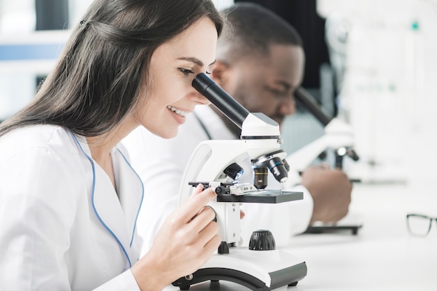 Cheerful medic woman looking at microscope