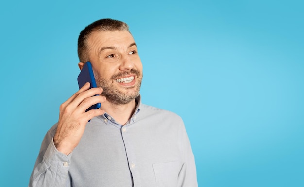 Cheerful Middle Aged Man Talking On Phone Over Blue Background