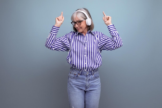 Cheerful middleaged woman with gray hair with headphones listens to music on a bright studio