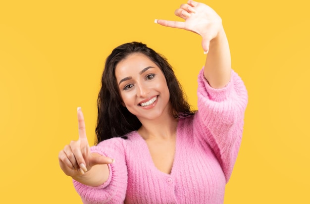 Cheerful millennial arab female in casual making lens gesture with hands isolated on yellow