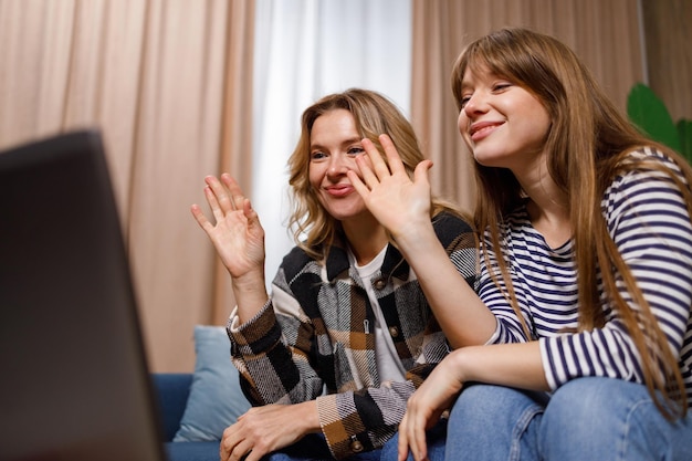 Cheerful mother and daughter are friendly waving to the laptop