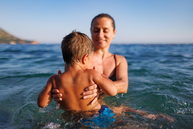 Cheerful mother plays with her son in the sea