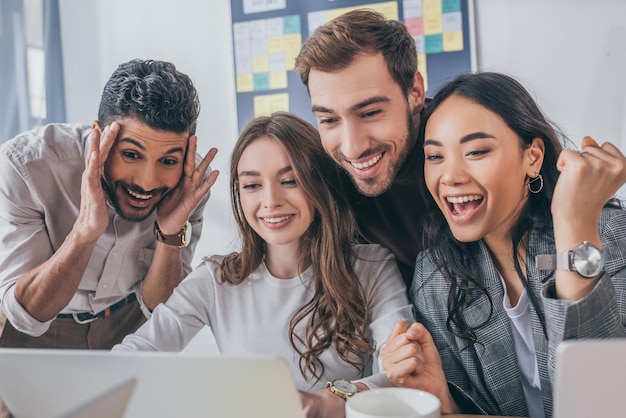 Cheerful multicultural businessmen and businesswomen looking at laptop in office