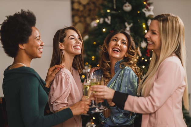 Cheerful multietnic girls having fun while toasting with champagne on Christmas or New Year's home party together.