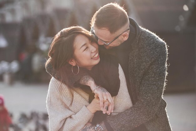 Cheerful multiracial couple embracing each other outdoors in the city. Asian girl with her caucasian boyfriend.