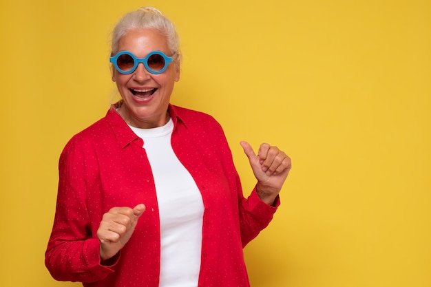 Cheerful old woman wearing trendy sunglasses isolated on yellow background laughing