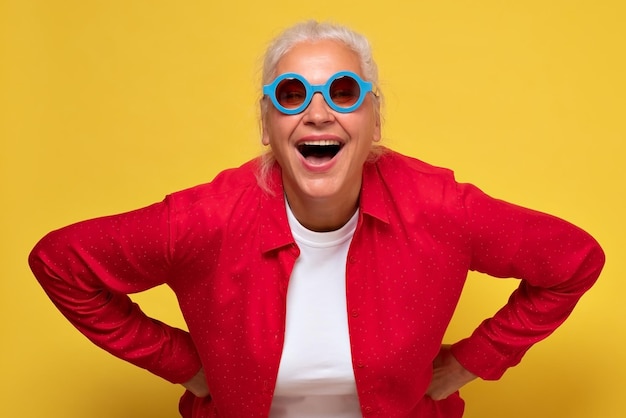 Cheerful old woman wearing trendy sunglasses isolated on yellow background laughing