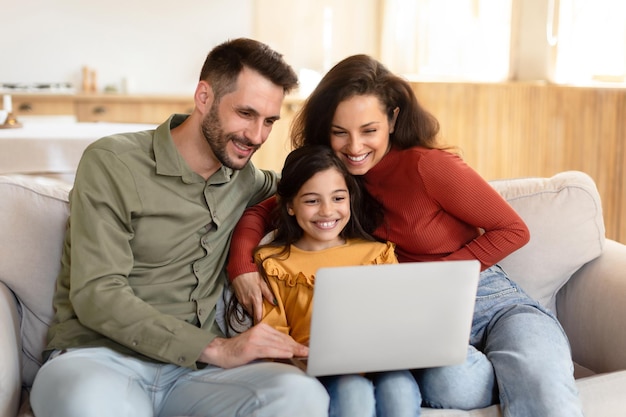 Cheerful parents and daughter using laptop spending time at home