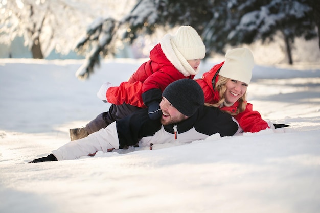 Cheerful parents and son are lying in the snow in the winter in the forest