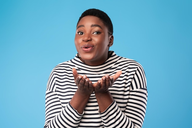 Cheerful PlusSized Black Woman Sending Air Kisses Over Blue Background