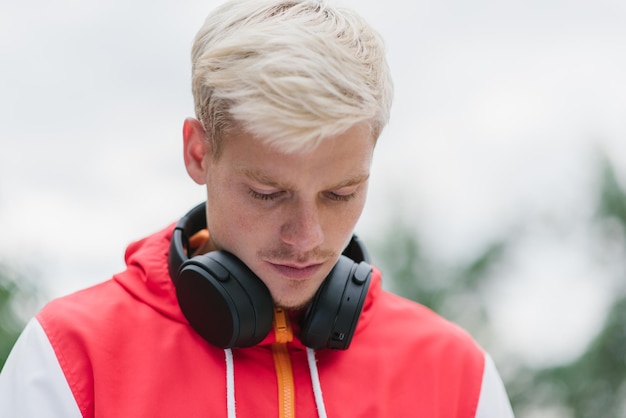 Cheerful portrait of modern blond man wearing red sportswear and headphones to listening the music in the park outdoor Young handsome man listening to music with headphones outdoor