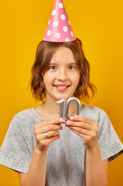 Cheerful positive ten years birthday girl in party hat