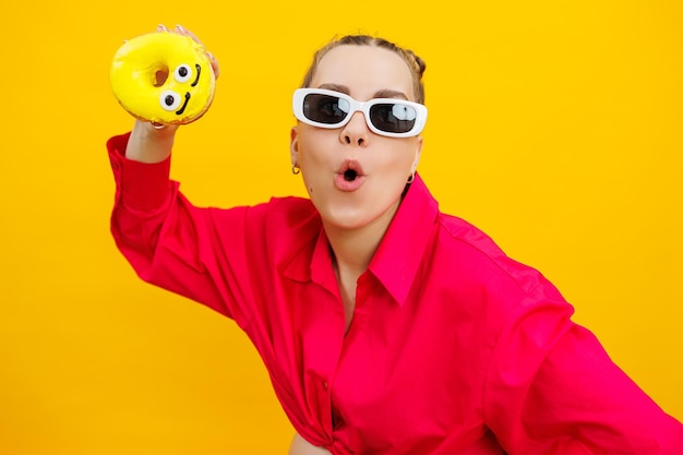 Cheerful pregnant woman holding a sweet yellow donut in her hand on a yellow background Expecting a child pregnancy and motherhood The concept of healthy and unhealthy food diet Junk food