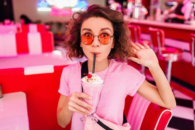 Cheerful pretty stylish smiling woman in retro vintage 50's cafe sitting at table