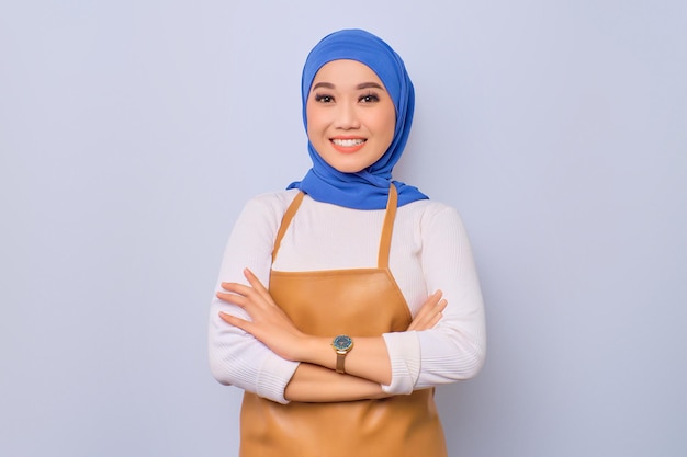 Cheerful pretty young barista girl in apron standing with crossed arms looking ready and confident isolated on white background