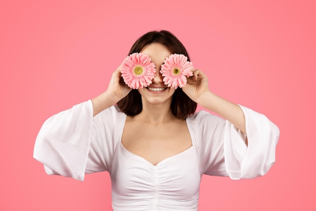 Cheerful pretty young european female puts flowers to her eyes like glasses has fun enjoy free time alone