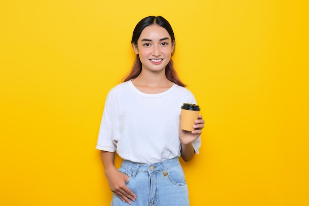 Cheerful pretty young girl in white tshirt holding coffee cup isolated on yellow background