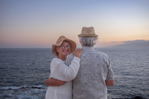 Cheerful senior couple hugging at the beach standing face the sea at sunset light Horizon over water