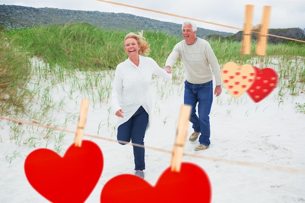 Cheerful senior couple running at beach against hearts hanging on the line