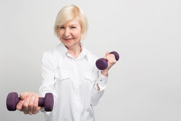 Cheerful senior lady exercising with light weights. She likes to do that because after exersices she feels much better.