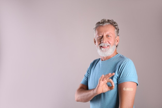 Cheerful senior man showing arm with bandage after vaccination on beige background Space for text