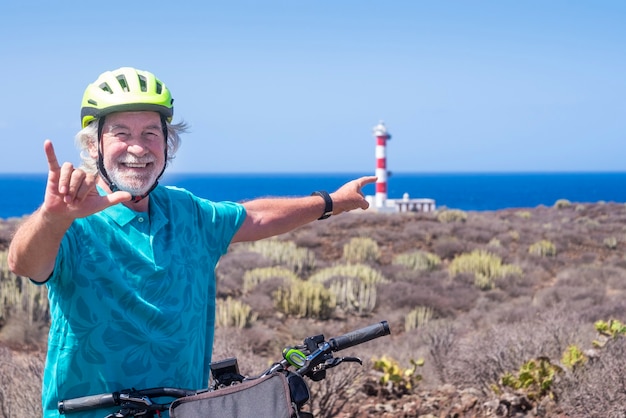 Cheerful senior man with yellow helmet enjoying excursion with bicycle close to a lighthouse