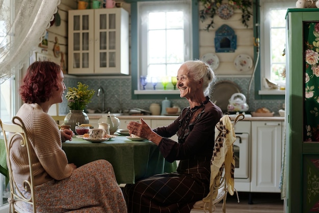 Cheerful senior woman in smart casualwear chatting with her granddaughter