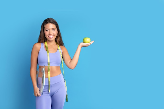 Cheerful slim young caucasian lady in sportswear with measuring tape show green apple