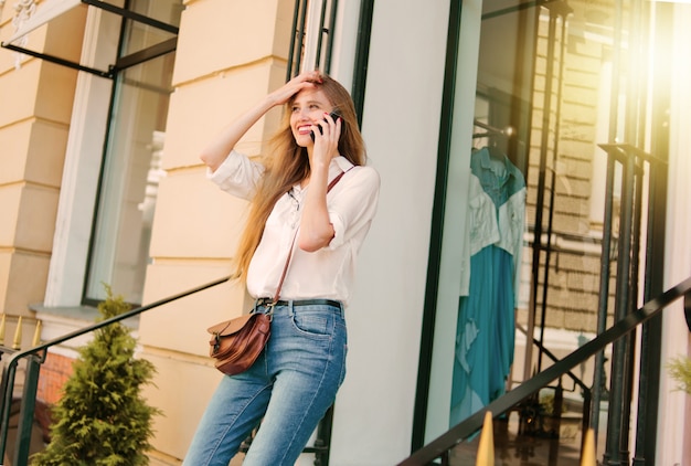 Cheerful smiling blond woman talking on the phone outdoors