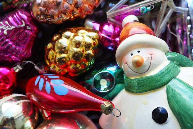 Cheerful smiling ceramic snowman in a green scarf and winter hat New Year and Christmas decorations tinsel Multicolored balls in the form of cones Festive interior decor New Year or Christmas