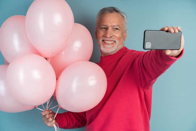 Cheerful, smiling, gray-haired man with balls on a blue wall