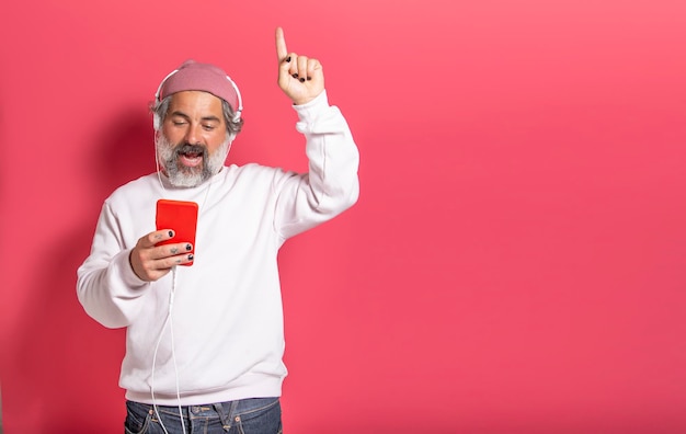 Cheerful and smiling handsome man listening to streaming music with headphones isolated on pink studio background with space for text