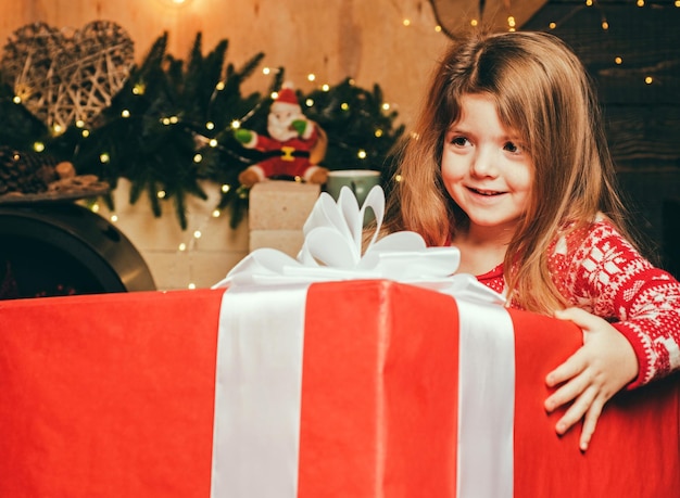 Cheerful smiling happy little cute girl holding gigantic gift present from Santa Christmas eve and m