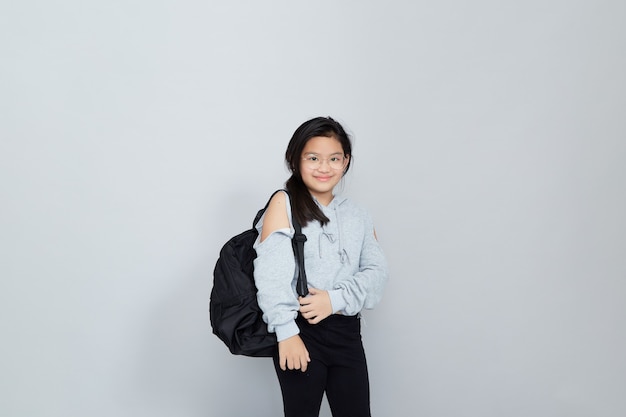 A cheerful smiling little Asian girl wears a school bag