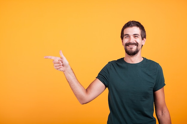 Cheerful smiling man pointing at his right at copyspace available for your advertisement or promotion. Isolated on orange backgorund in studio.