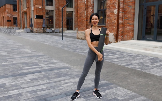 Cheerful sporty woman with yoga mat outdoors