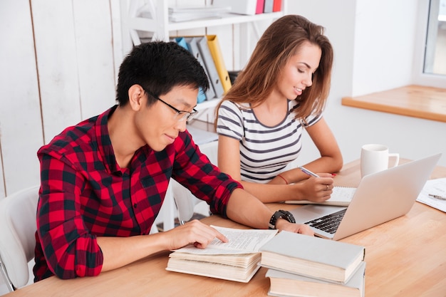 Cheerful students working in classroom. Girl writing and sitting near laptop