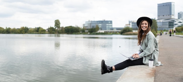 Cheerful stylish woman freelancer working online on the embankment with a laptop in her hands