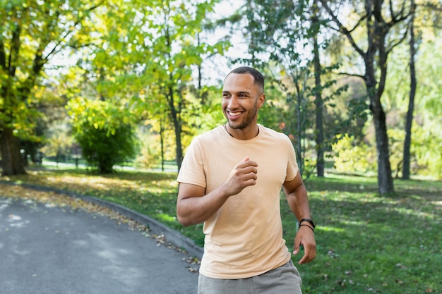 Cheerful and successful hispanic man jogging in the park man running on a sunny day smiling and