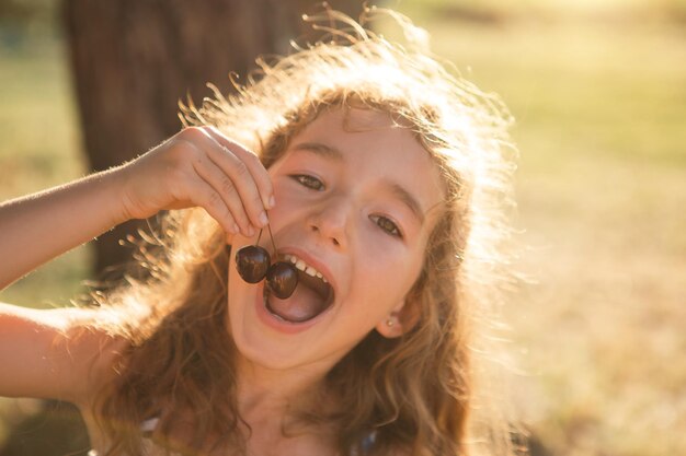 A cheerful sweet girl with cherry berries in her mouth Funny summer portrait of a child with a cherry gifts of summer summer time