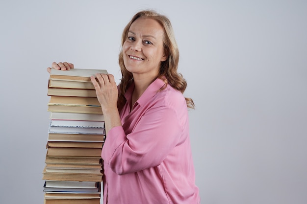 Cheerful teacher in a pink blouse stands next to a large pile of books portrait