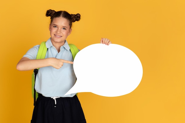 Cheerful teen european girl with backpack points finger at abstract cloud for words and thoughts