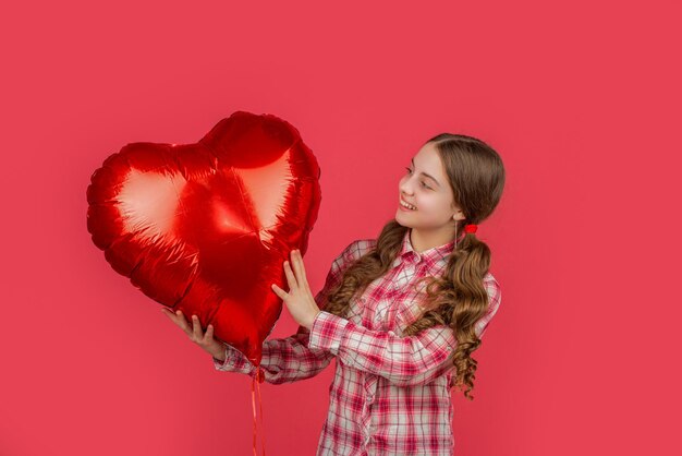 Cheerful teen girl hold love heart balloon on red background